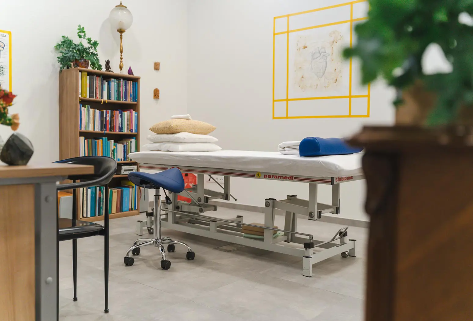 Behandelruimte met behandeltafel, boekenkast en gele lijnen op de muur